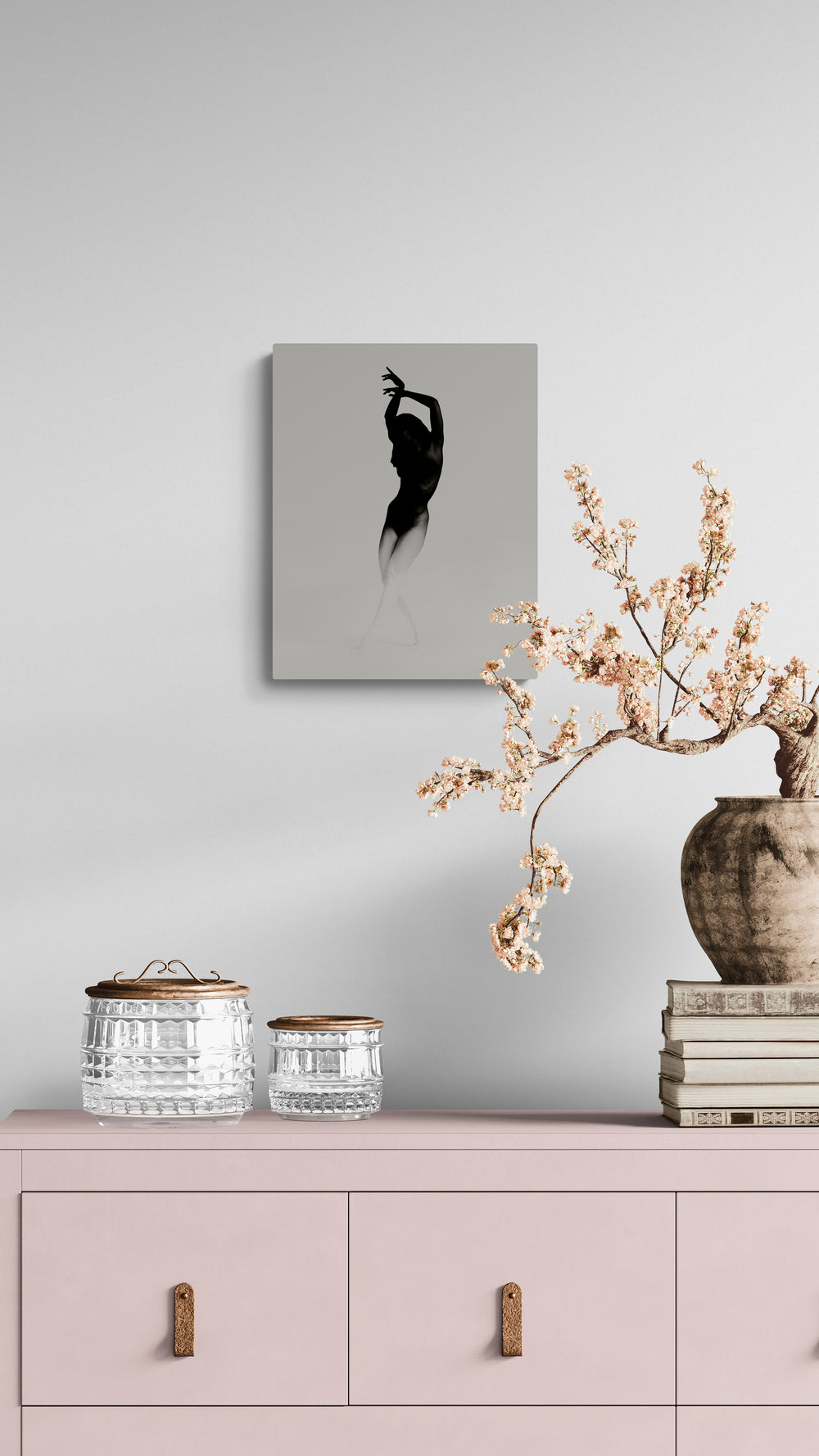 Decorative setup with a painting, vases, and books on a pink cabinet against a light gray wall.