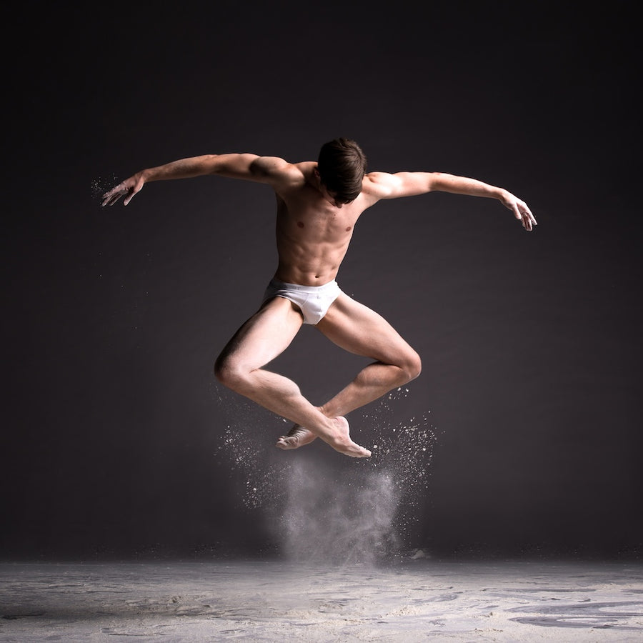 Male dancer suspended in mid-leap above a rising cloud of white powder on a dark stage in the Cloud Dancer – Powder Leap fine art dance photograph.