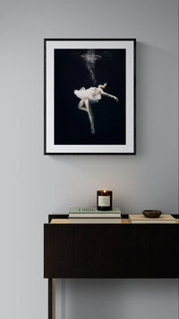 Ethereal Descent framed print hanging above a dark modern console table with books and a candle in a minimalist interior.