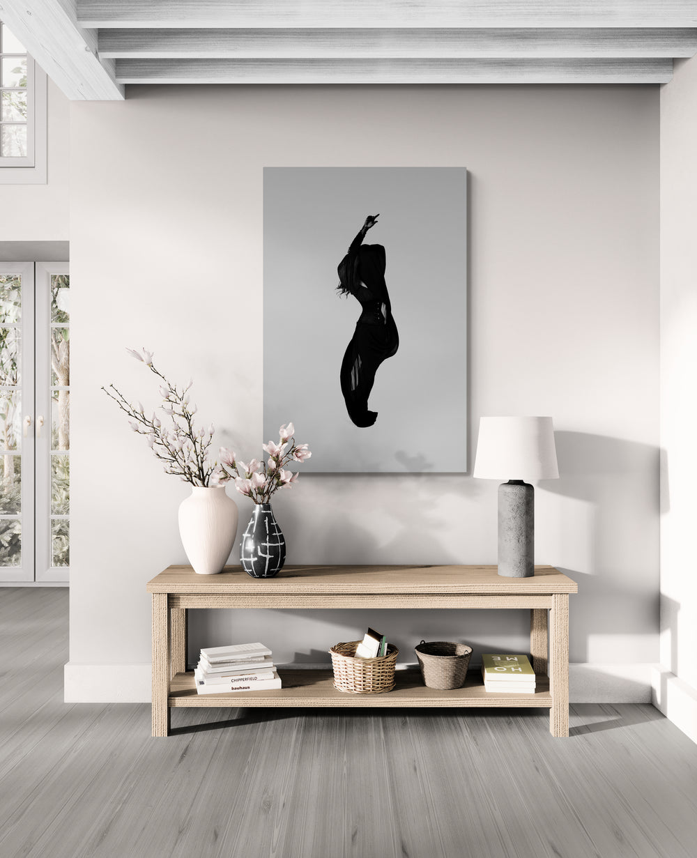 Modern living room with a silhouette art piece on the wall above a wooden console table. Artwork presenting a twisting torso under sheer fabric; collectible limited edition shown on wall for design professionals seeking dynamic fine-art.