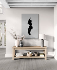 Modern living room with a silhouette art piece on the wall above a wooden console table. Artwork presenting a twisting torso under sheer fabric; collectible limited edition shown on wall for design professionals seeking dynamic fine-art.
