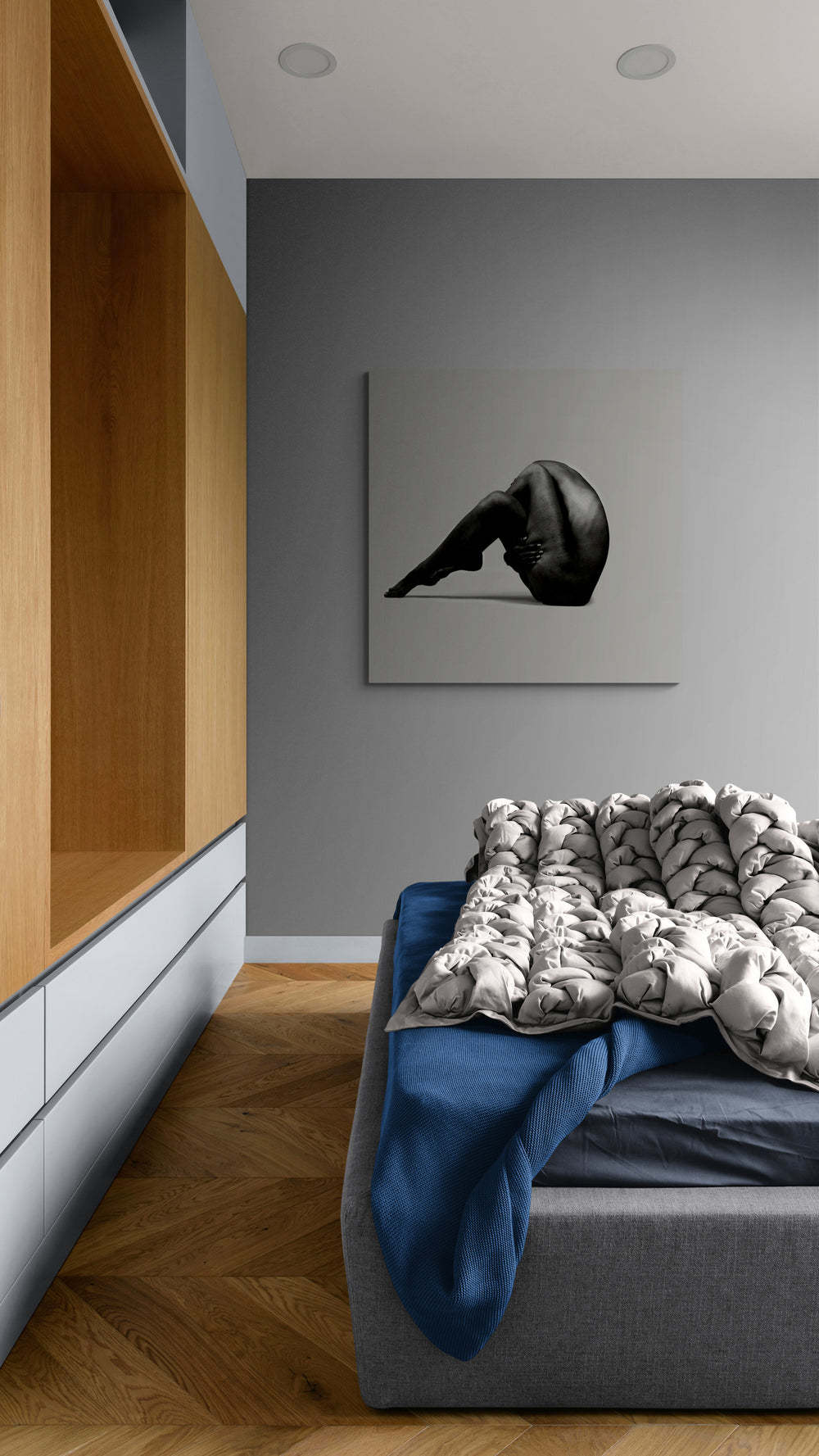 Monochrome figure in a sculptural side coil, displayed as framed wall art in a modern bedroom with wooden shelves, gray walls, and a bed with patterned blanket; archival, limited edition print ideal for interior designers seeking premium contemporary photography and collectible wall decor.