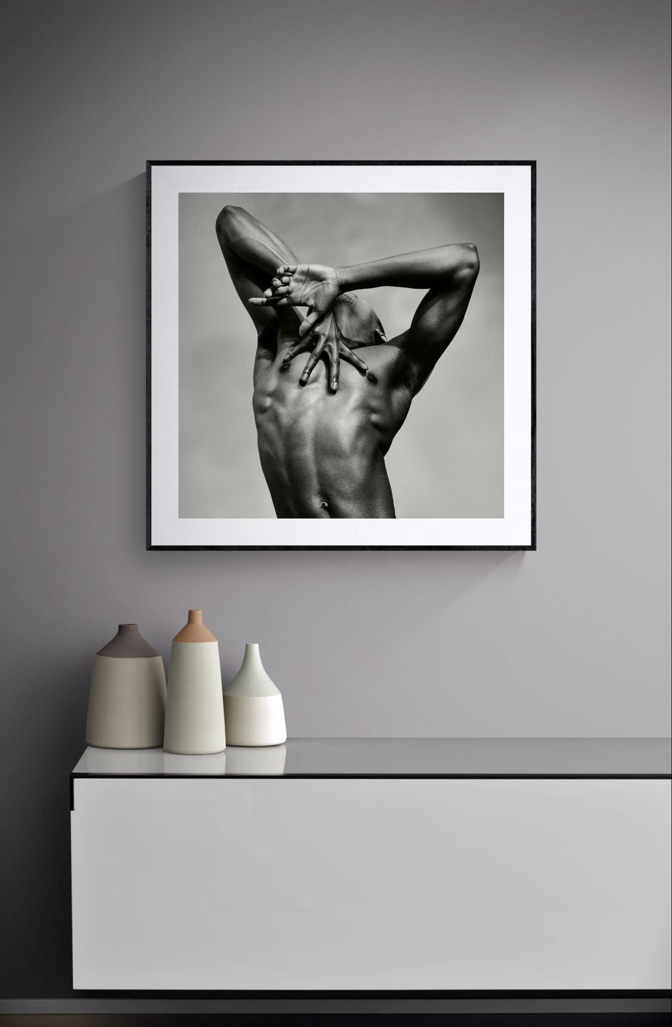 Framed monochrome artwork J. by Sasha Onyshchenko hanging above a modern cabinet with ceramic vases in a minimalist grey interior.