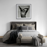 Large framed J. print by Sasha Onyshchenko showcased above a light grey upholstered bed in a luxury minimalist bedroom with layered neutral textiles.