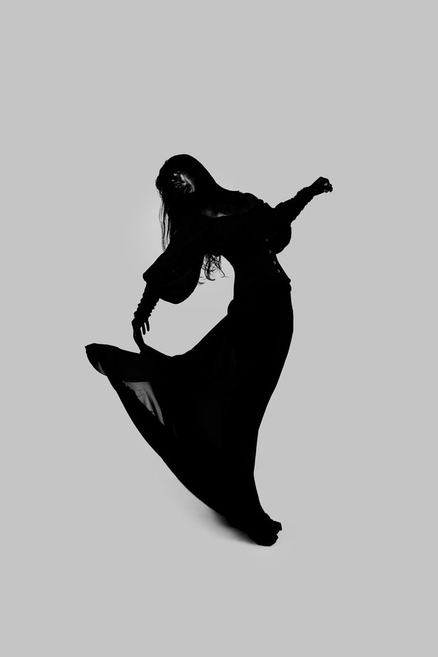 Dark dress in motion as the body arcs upward; fabric traces the path of lift and acceleration.