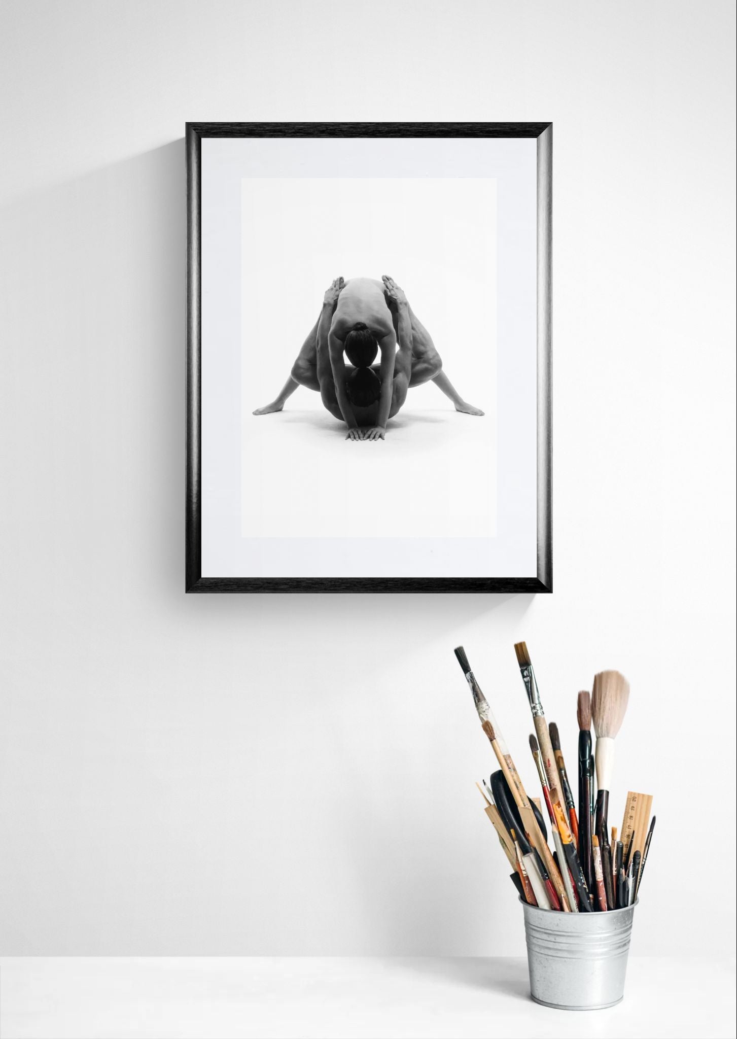 Framed fine art nude dance photograph presented on a white studio wall with artist brushes in the foreground.