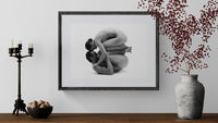 Framed black and white artwork of a person embracing a pillow on a wall with decorative elements below.