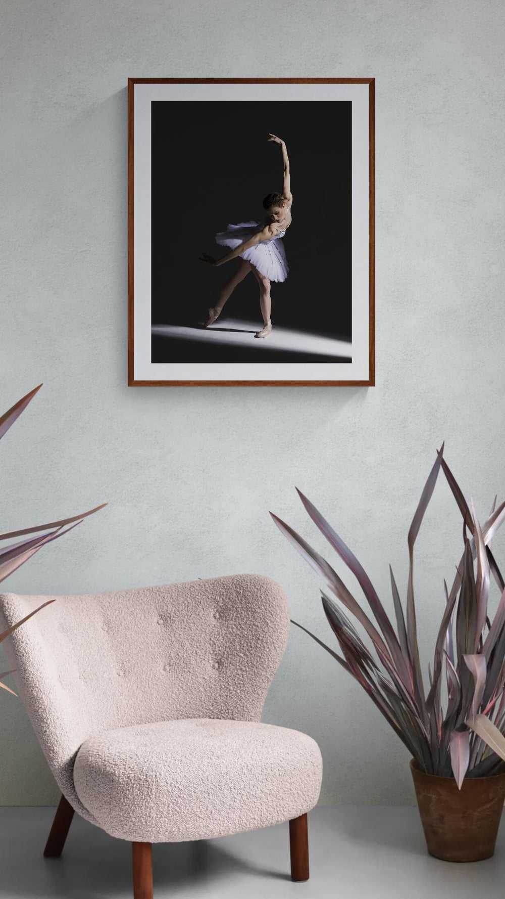Framed photograph of a dancer in a dark setting above a chair with plants on either side.
