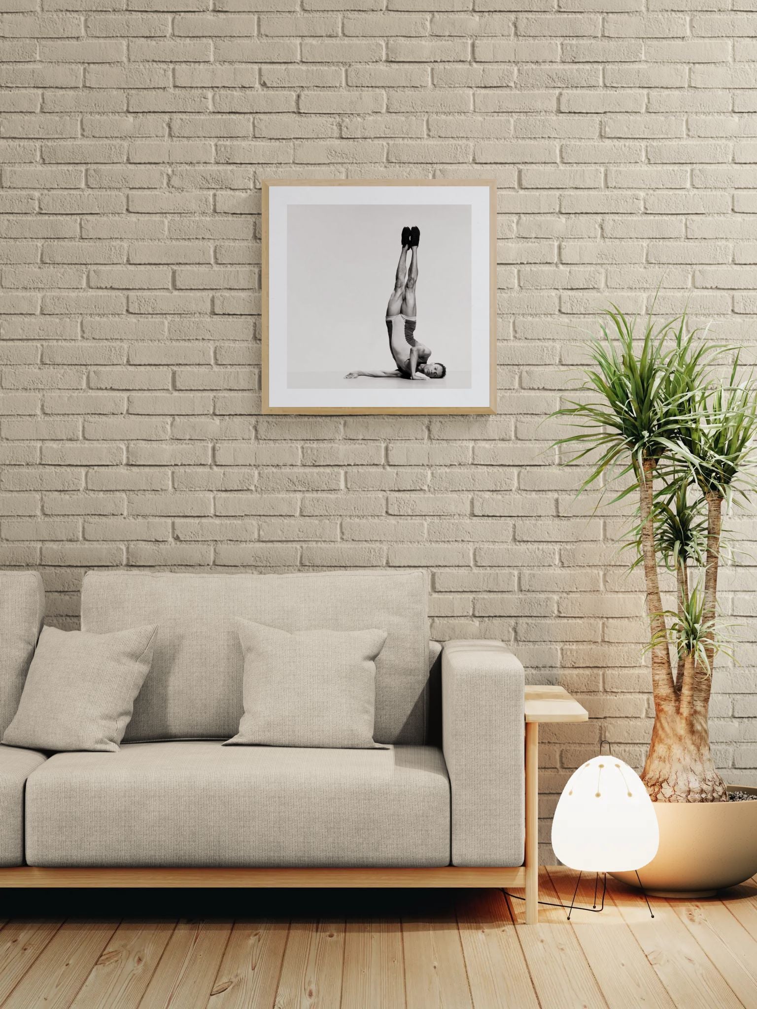 Modern living room with a gray sofa, framed artwork, and a plant against a brick wall.