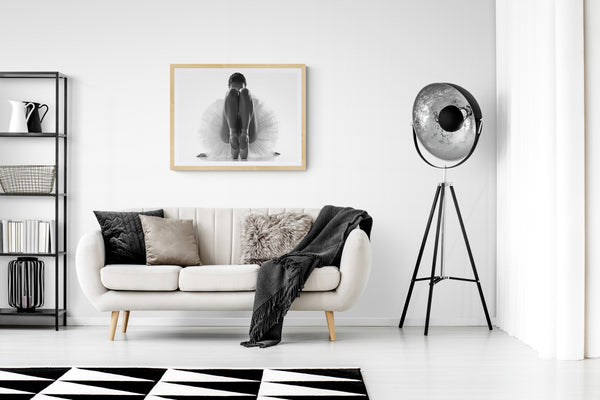 Modern living room with a white sofa, black and white rug, and decorative lamp. Framed ballerina dance print in neutral tone exhibited on the wall.