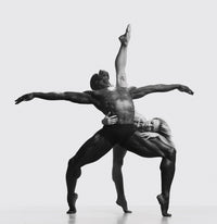 Black-and-white photograph of two dancers forming a crossed, sculptural pose, one standing with arms extended, the other leaning with an elevated leg.