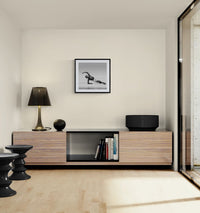 Modern living room corner with a low wooden console, lamp and decor objects, featuring a framed square black-and-white dance photograph on the wall above.