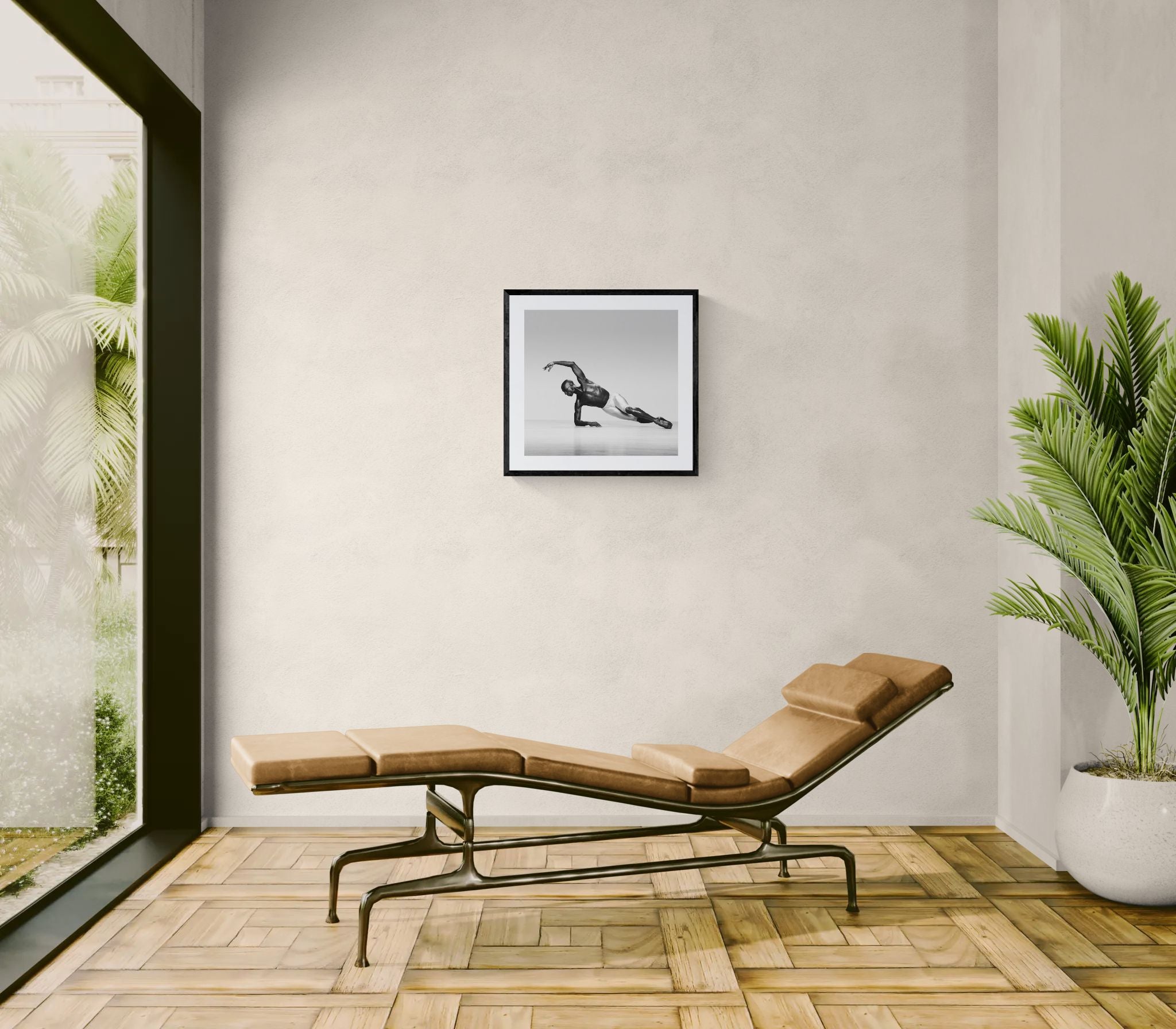 Sunlit room with a reclining lounge chair and large potted plant, featuring a framed square black-and-white dance photograph on the wall.