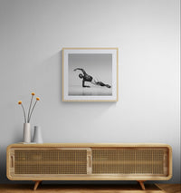 Neutral interior with a cane-front wooden console and slim vases, with a framed square black-and-white dance photograph hanging above.