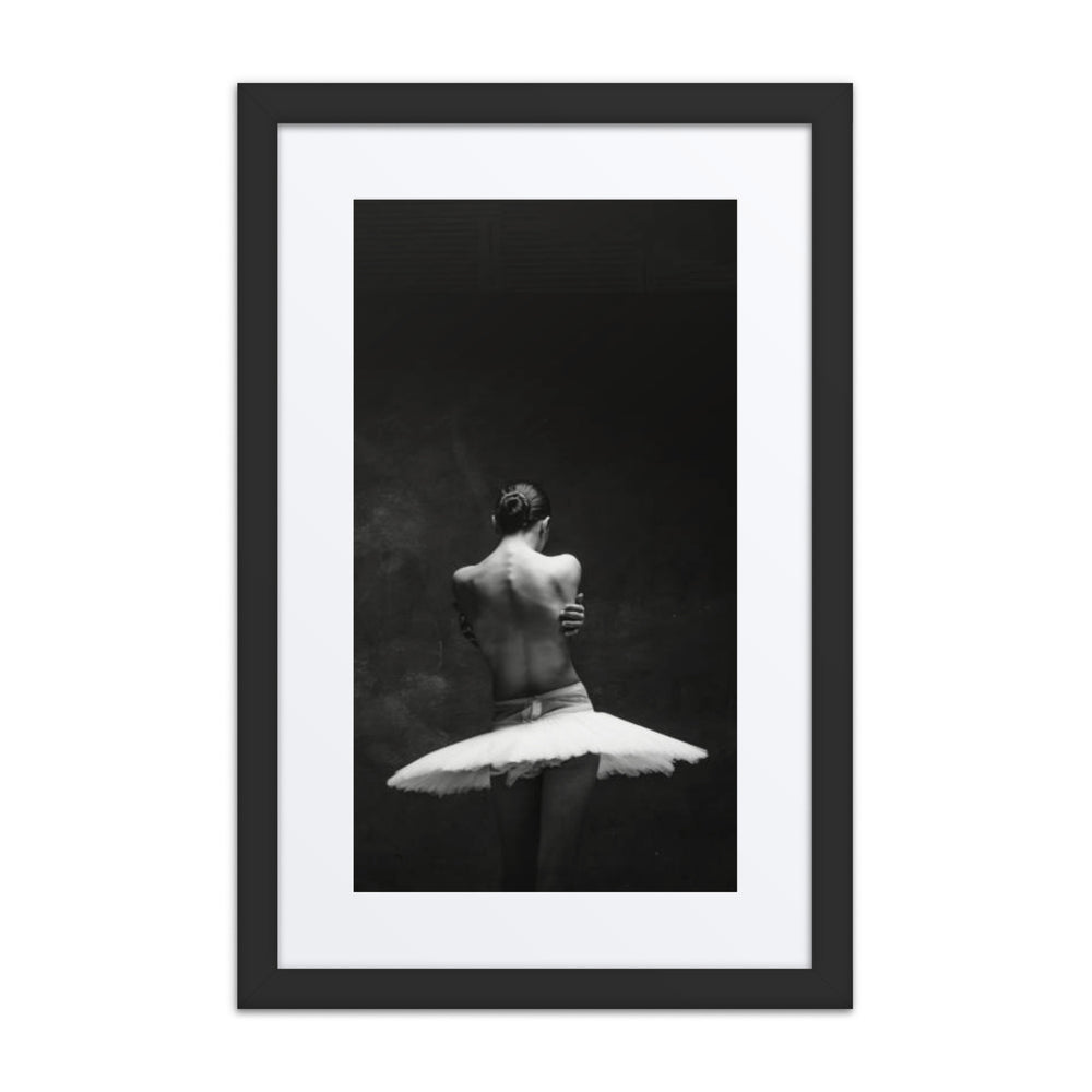 A monochrome photograph capturing a ballerina from behind, her arms crossing inwards as if in a self-embrace, set against a dark, minimalist background. A poignant depiction of introspection and solitude in dance.