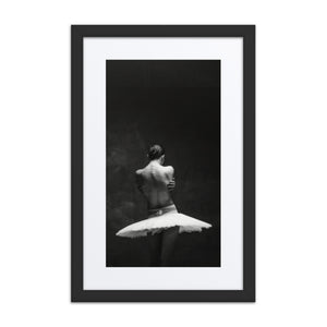 A monochrome photograph capturing a ballerina from behind, her arms crossing inwards as if in a self-embrace, set against a dark, minimalist background. A poignant depiction of introspection and solitude in dance.