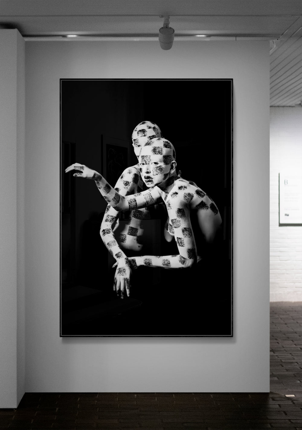 Framed black and white artwork of a person with a patterned outfit on a wall in an art gallery.