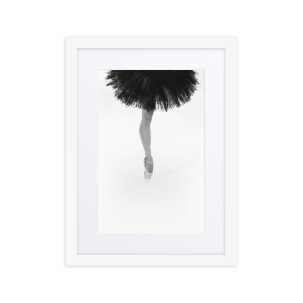 A black and white fine art photograph of a ballerina en-pointe wearing a black tutu, framed in a gallery-style black frame with a white border.