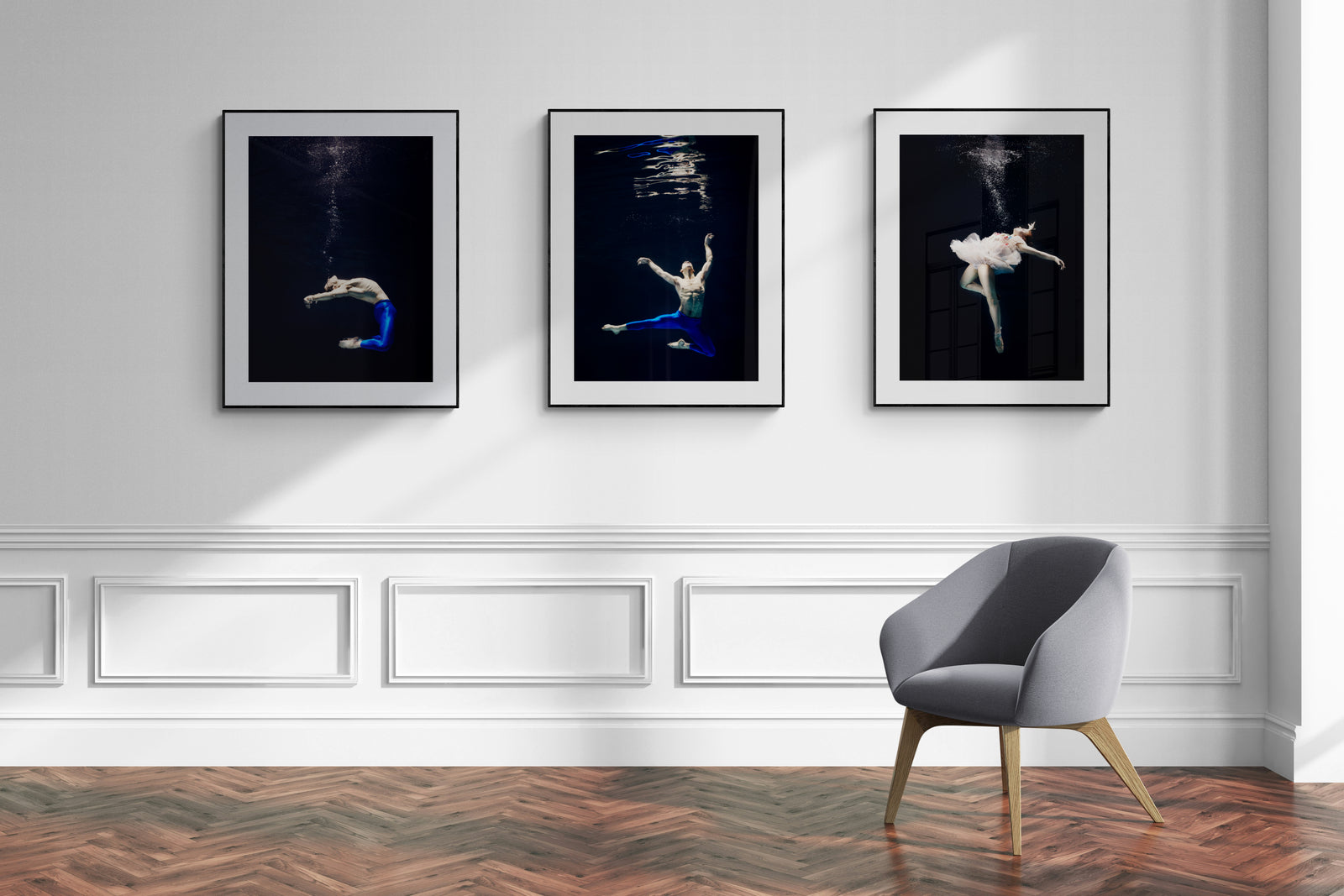 Underwater dance photography triptych in black frames with white mats, mounted on a classic white wall above herringbone flooring.