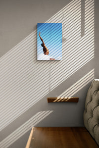 Black male dancing in the nature. His hand is oriented up onto the blue sky. We see him from behind. his armpit is glowing into the sunlight. Photo print on a wall.