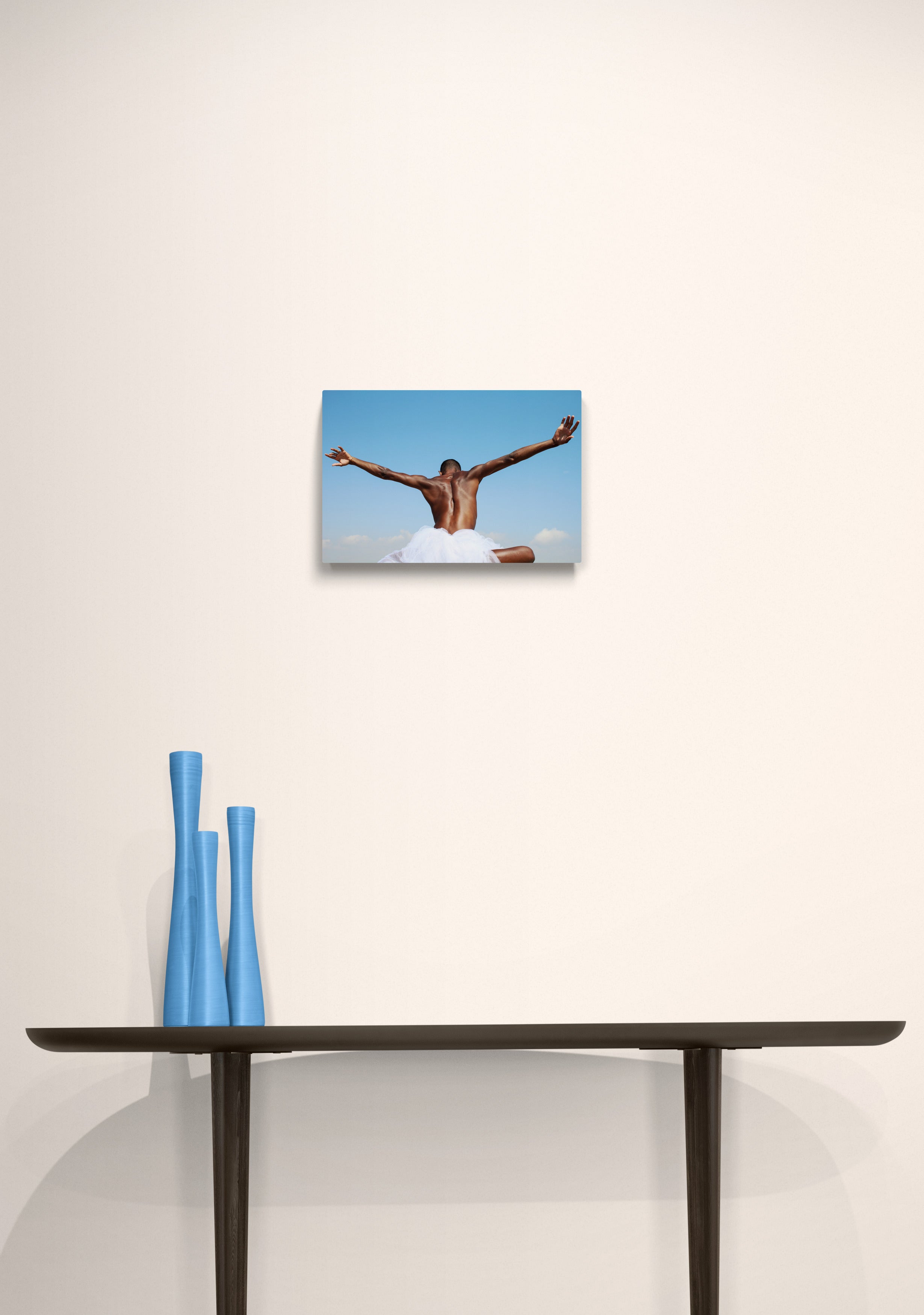 With open arms, we see a black male spreading his hands like wings into the blue sky. Art print on a white wall.