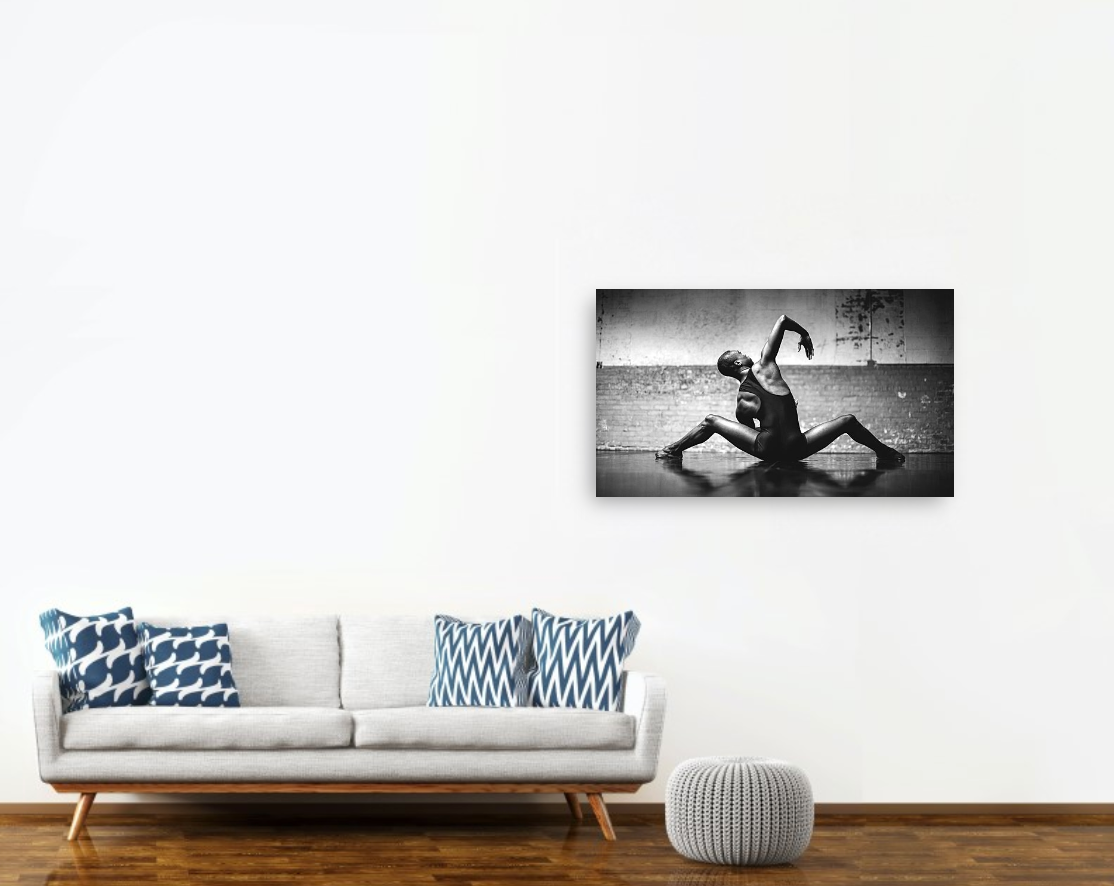 a couch and a white wall with a photo print hanging depicting a sexy male dancing performing a movement on the floor